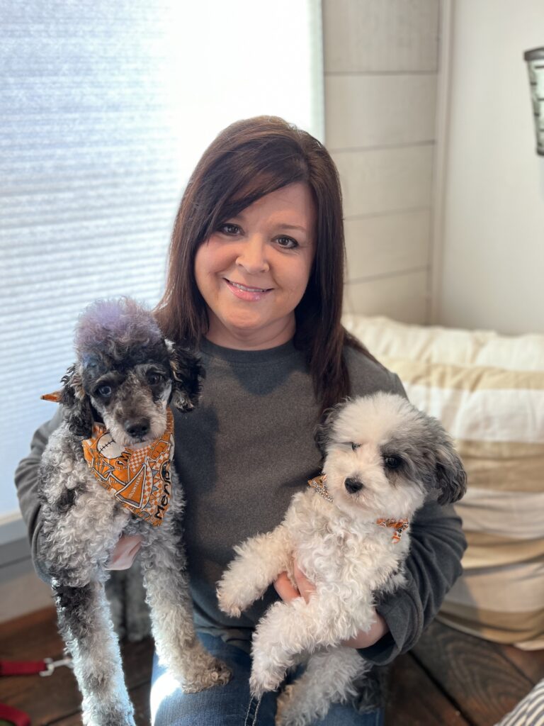 Woman sitting and holding two gray and white dogs in her arms.